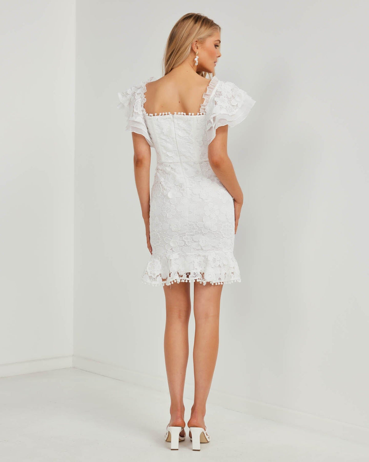 Half Open Back Design of Side Image showcasing Slimming Fit of Twosisters The Label White Floral Lace Mini Dress featuring Off The Shoulder Sweetheart Neckline and Frilled Hem Sleeves and Skirt