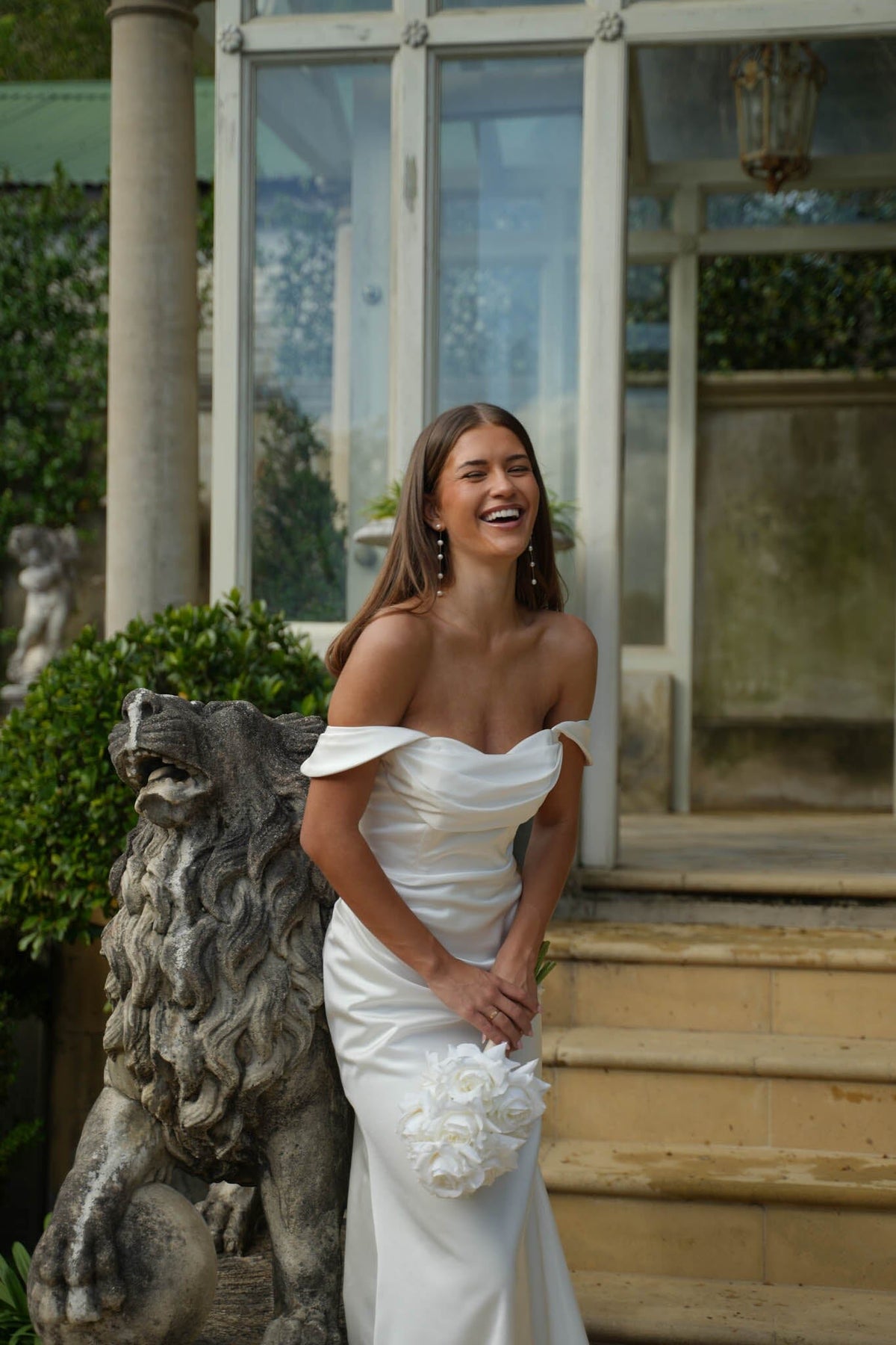 Bride in a white off the shoulder wedding dress standing outdoors with decorative elements in the background