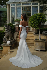 Woman in a white off-shoulder wedding dress standing in a garden setting.