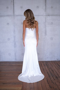 Back image of white bustier strapless fitted stretch satin wedding gown with high side slit and moderate train