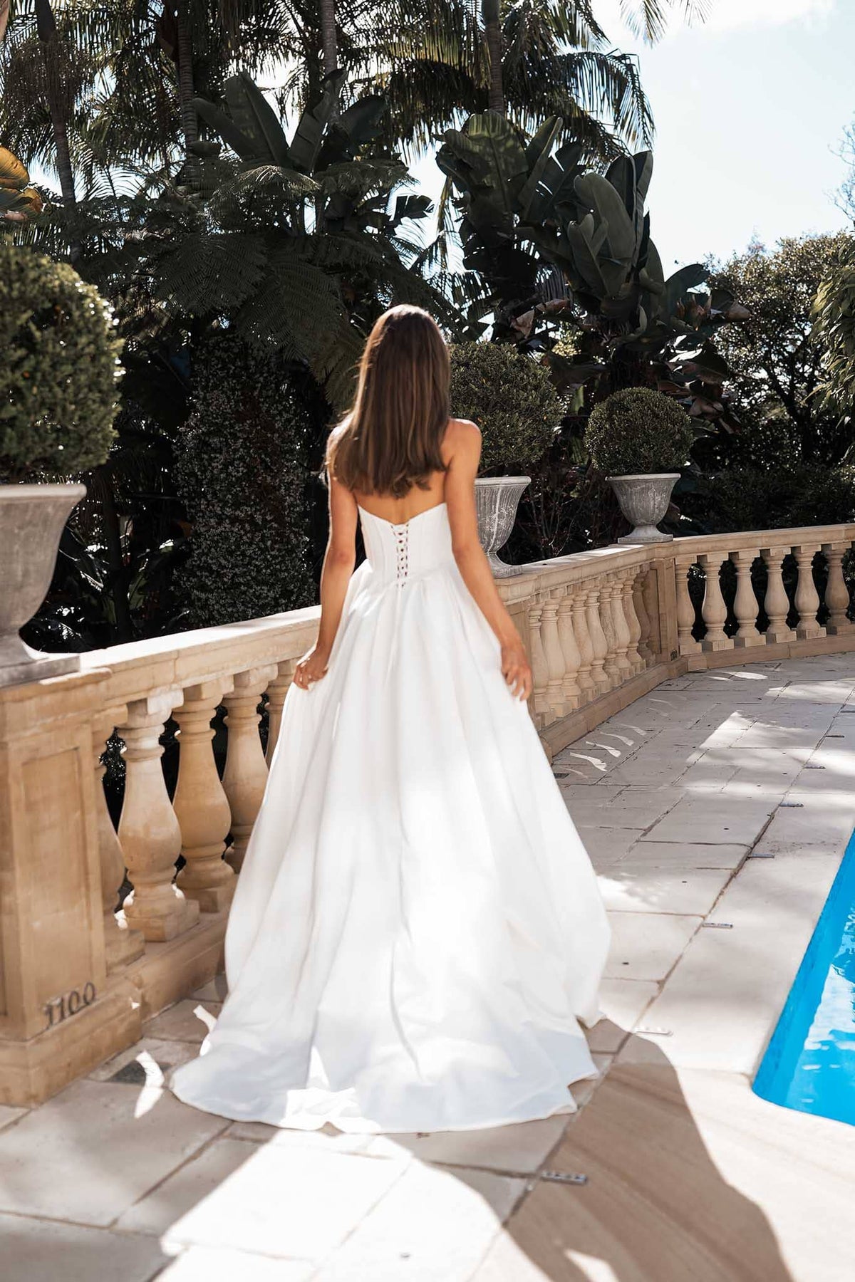 Lace up back design of white strapless ballgown wedding dress with a Basque waist, draped neckline and leg slit