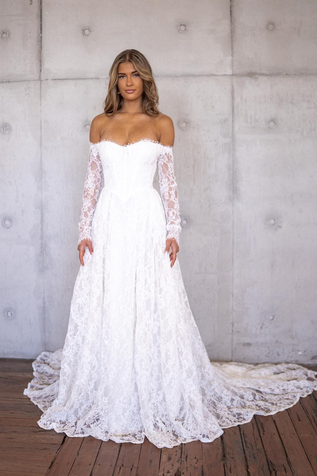 Ivory White Off The Shoulder Long Sleeve Lace Wedding Gown featuring Sweetheart Neckline with Lace Trimming Detail, Sheer Long Sleeves, Corset Bodice, Basque Waistline, Full A-line Skirt and Long Train.