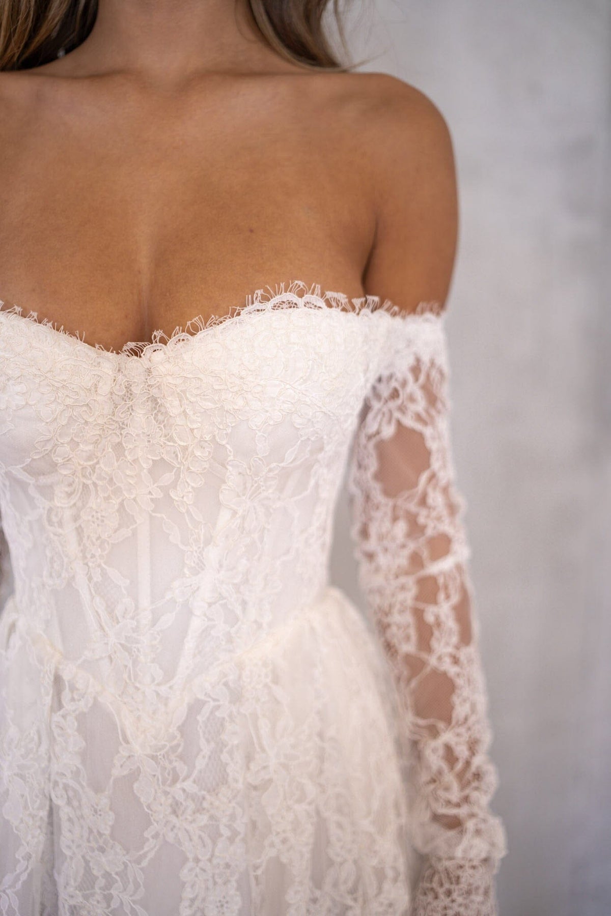 Close Up Image of Ivory White Off The Shoulder Long Sleeve Lace Wedding Gown featuring Sweetheart Neckline with Lace Trimming Detail, Sheer Long Sleeves, Corset Bodice, Basque Waistline, Full A-line Skirt and Long Train.