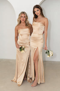 Two Bridesmaids wearing Neutral Gold Champagne Coloured Strapless Satin Maxi Dress with Draped Detail at Bust and Side Slit