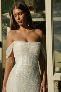 Bride wearing an off-shoulder, beaded ivory white wedding dress with corset bodice standing in front of a decorative door