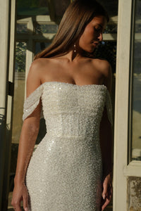 Woman wearing a sparkling off-shoulder wedding dress standing indoors.