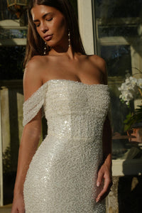 Woman wearing a sparkling off-shoulder wedding dress in an outdoor setting.