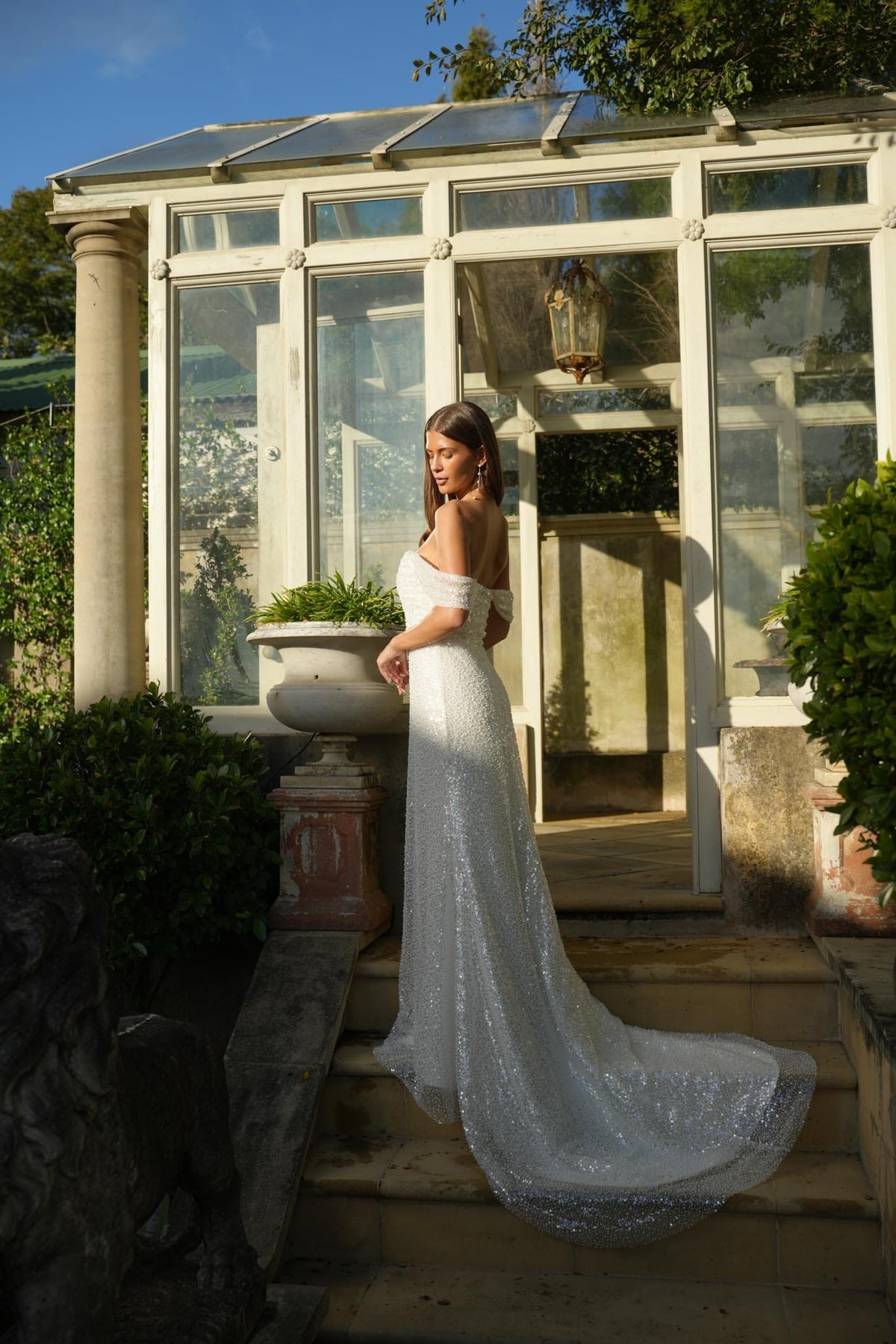Woman in a white sparkly wedding dress standing in front of a greenhouse