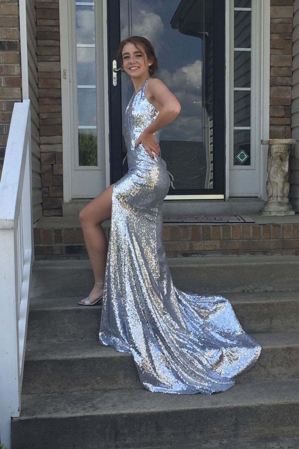 Customer wearing silver Estellina sequin sleeveless evening long gown with deep V neckline, thigh-high slit, halter-neck strings, open back, and long train