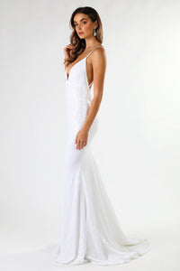 Side shot of fitted white sequin formal wedding sleeveless long gown featuring deep V neck, thin shoulder straps, backless design, and long train