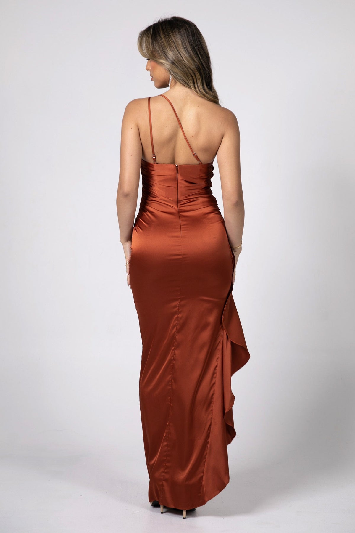 Back Image Showing 2 Adjustable Straps at the Back of Form Fitting Satin Maxi Dress with One Shoulder Neckline, Gathering Detail at Waist and Frill Hemline in Burnt Orange Color